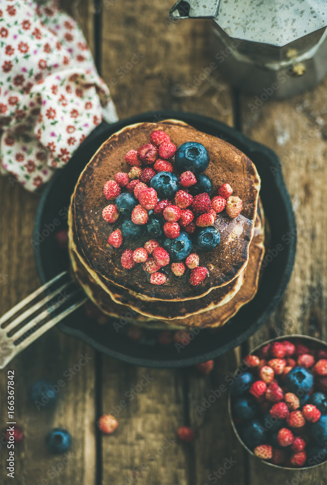 Sweet breakfast with pancakes with fresh forest berries and honey in cast iron pan over rustic woode