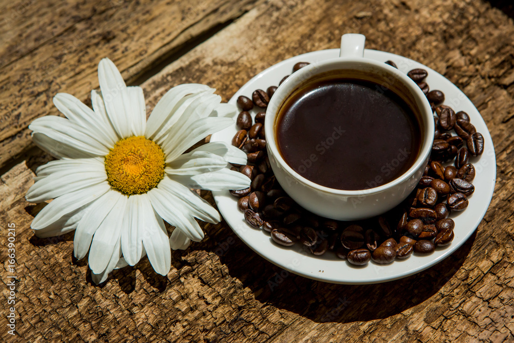 Coffee cup and fried Coffee beans on a wooden table with beautiful white flowers on a wood backgroun