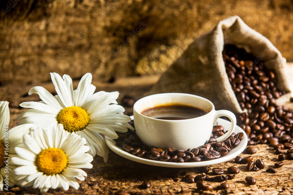 Coffee. A hot cup of coffee and roasted coffee beans on a wooden table. Dark background