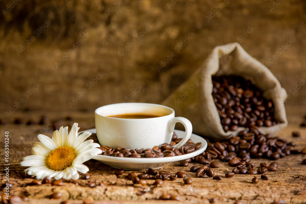 Coffee cup and coffee beans on a wooden background with chamomile