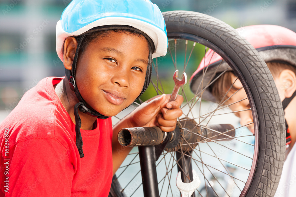 African boy repairing bicycle wheel with spanner