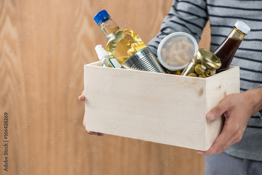 Volunteer with donation box with food stuffs on wooden background