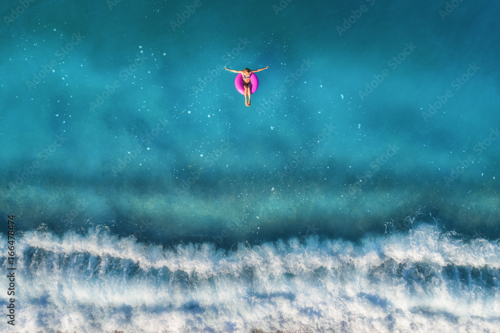 Aerial view of young woman swimming on the pink swim ring in the transparent turquoise sea in Oluden