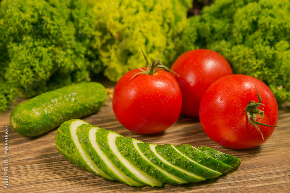 Fresh vegetables. Tomatoes and cucumbers on a wooden table. Green salad in the background. Healthy f