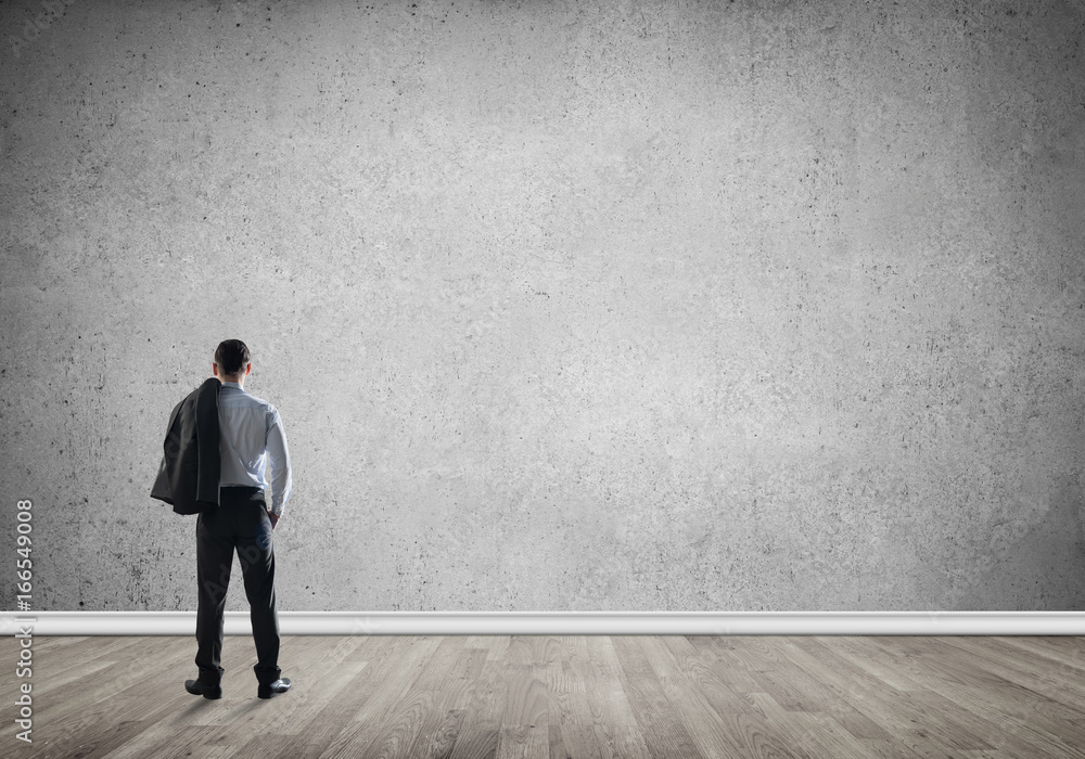 Businessman threw his jacket over his back and looking at blank concrete wall