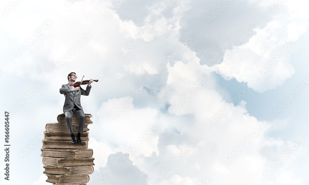 Handsome violinist in blue day sky on pile of books play his melody