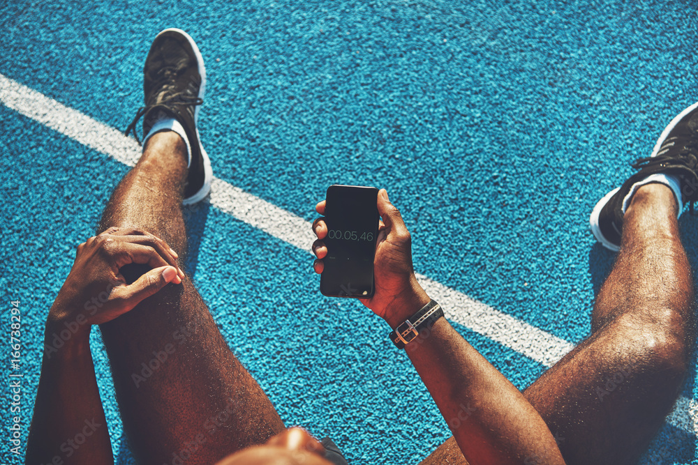 Young runner checking his lap time on a cellphone