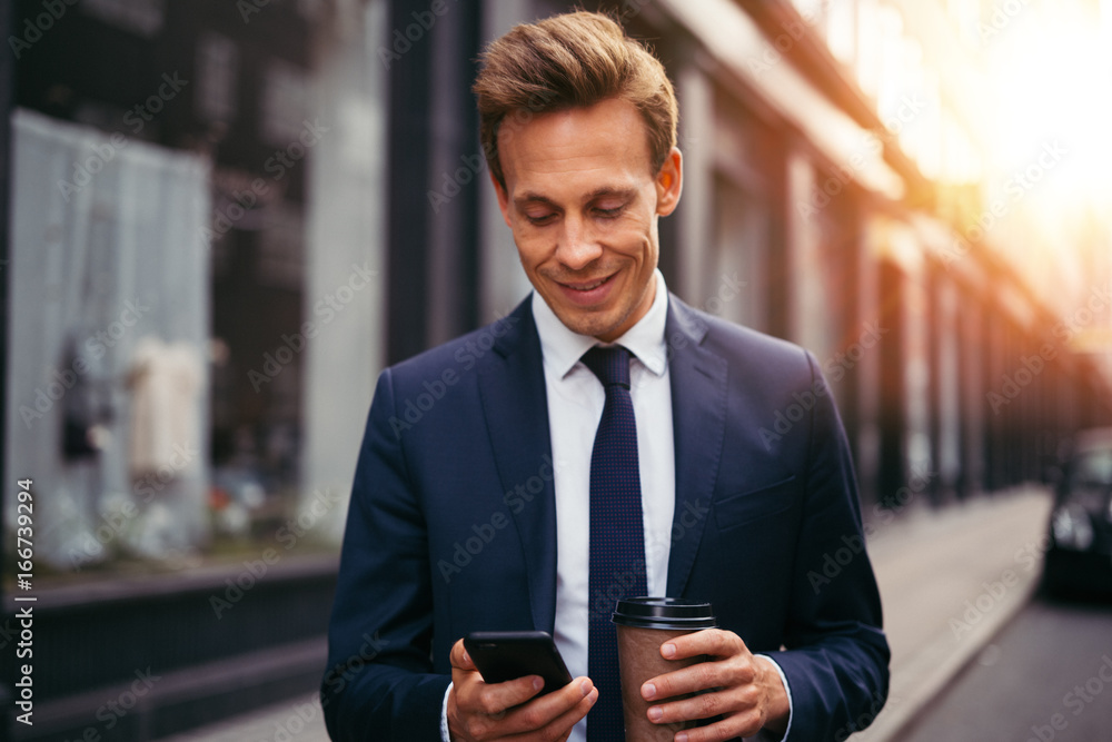 Smiling businessman drinking coffee and reading texts in the cit