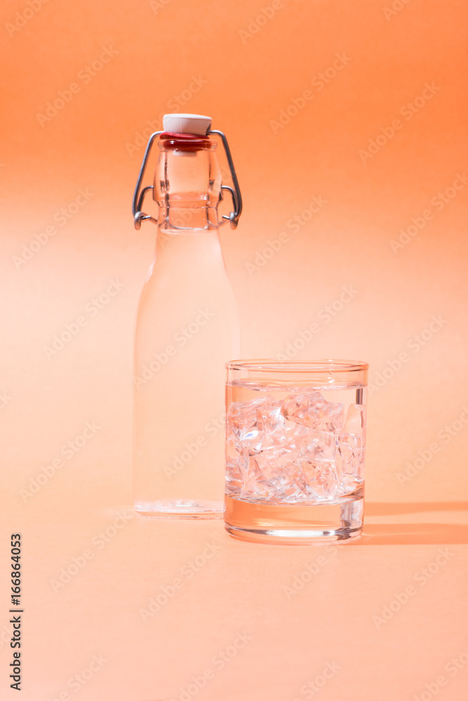 Drinking water in a bottle and glass of ice over orange background.