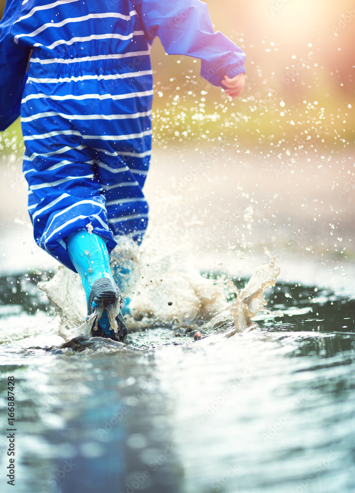 雨天孩子穿着雨鞋在水坑里行走