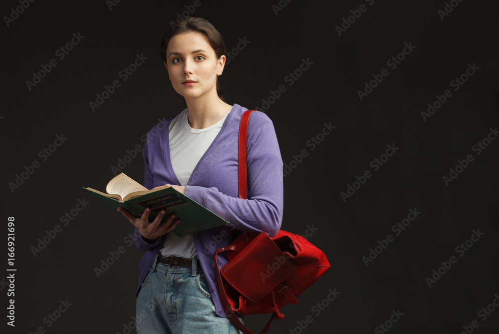 attractive female student stand with red backpack and leafing education book isolated on black backg