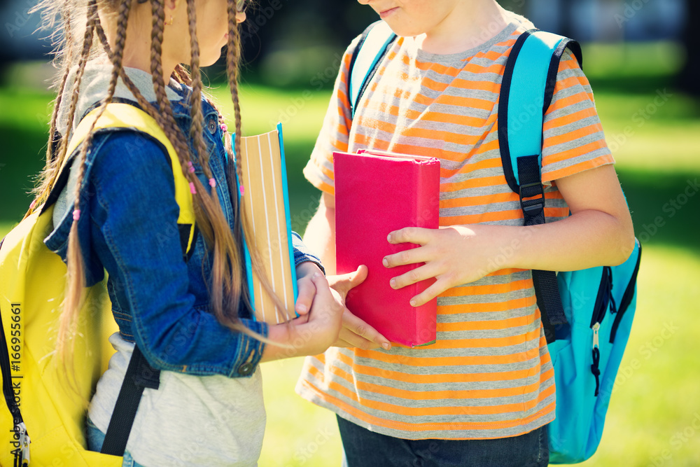 Children with rucksacks standing in the park near school. Pupils with books and backpacks outdoors