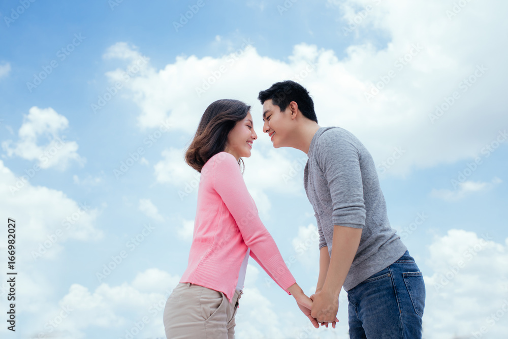 Young beautiful woman and asian man laugh against the dark blue sky with clouds