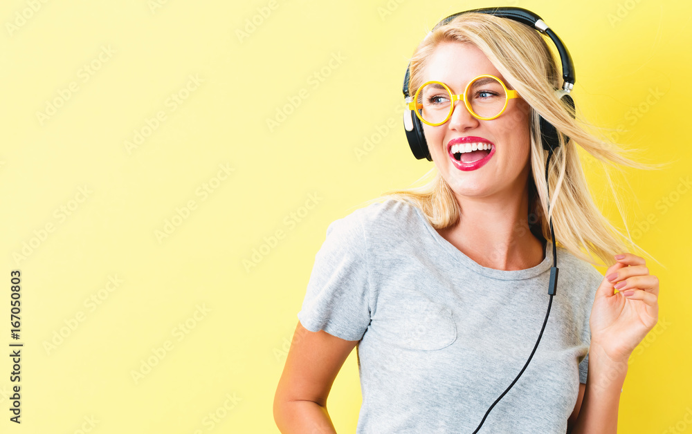 Happy young woman with headphones on a yellow background