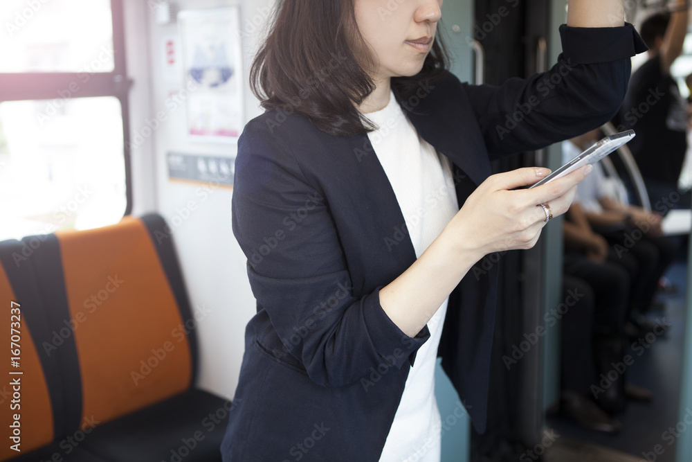 A woman is caught on a hanging leather inside a train and watching a smartphone