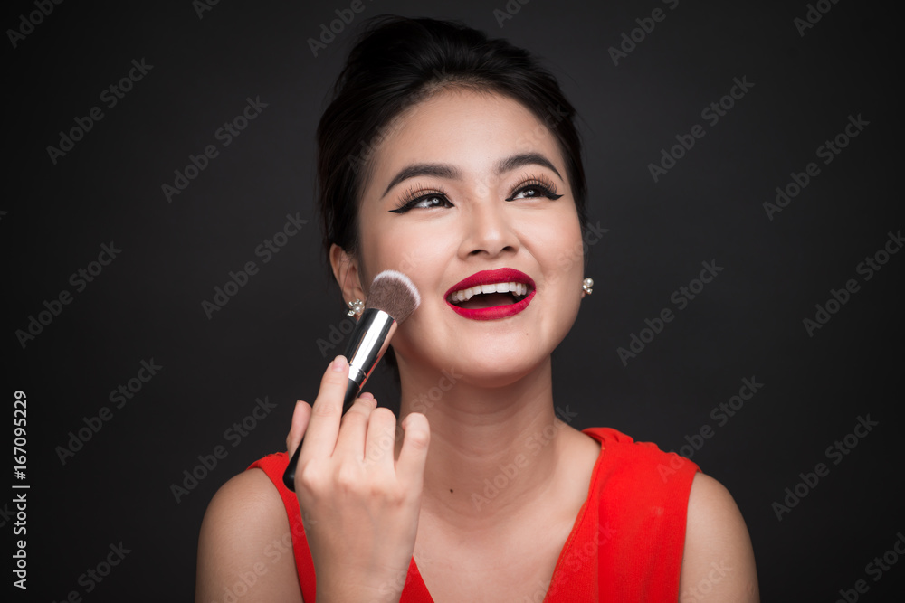 Cosmetic powder brush. Asian woman applying blusher on her cheeks with perfect make-up and red lips