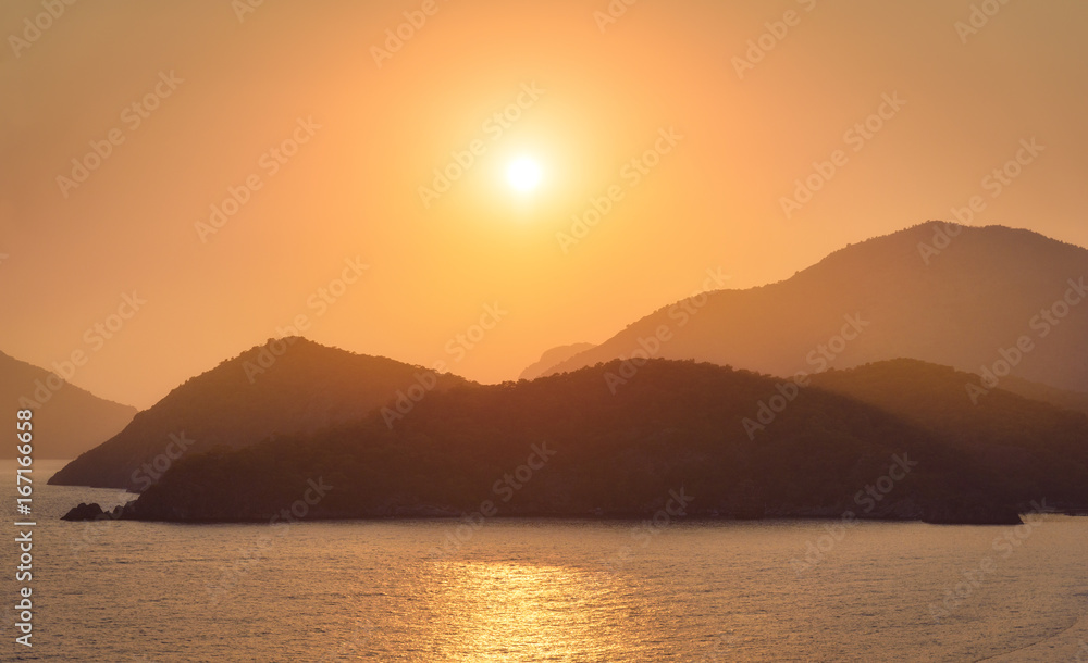 Beautiful seascape with silhouettes of mountain ridges, water, islands, and orange sky in summer at 