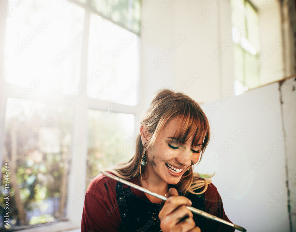 Female artist smiling with paint brush in studio