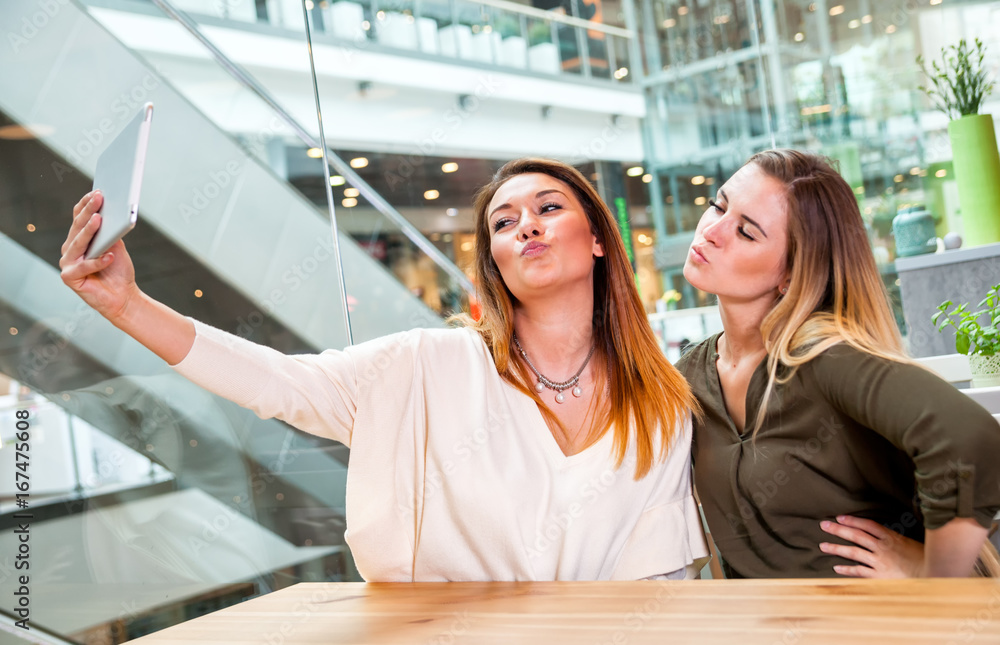 Two woman girls taking selfie with digital tablet in cafe at shopping mall