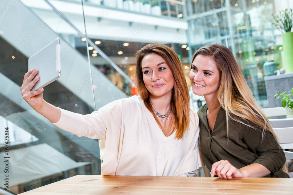 Two woman girls taking selfie with digital tablet in cafe at shopping mall