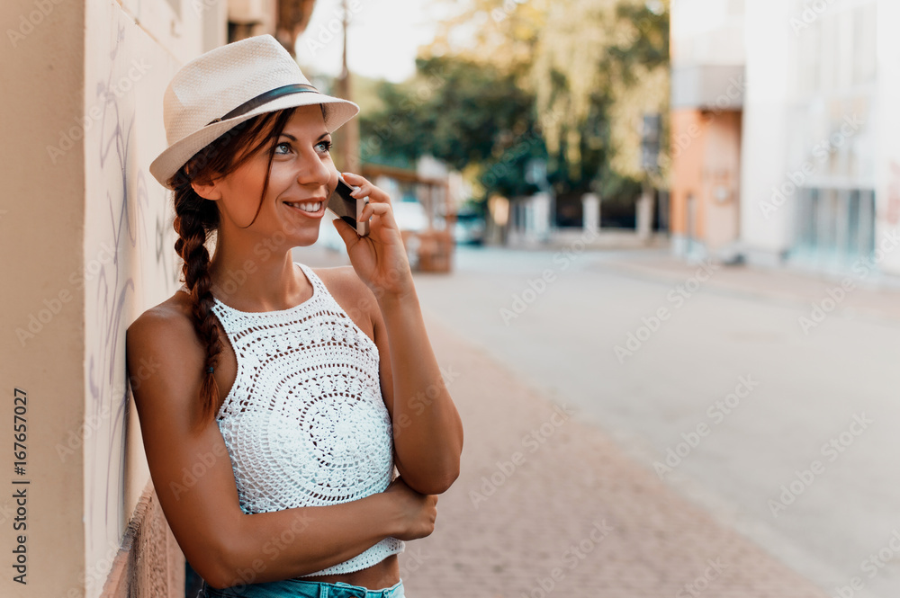 Woman with hat talking by phone outdoors in city street.