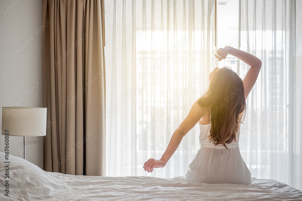 Asian woman wake up in the morning, sitting on white bed and stretching, feeling happy and fresh