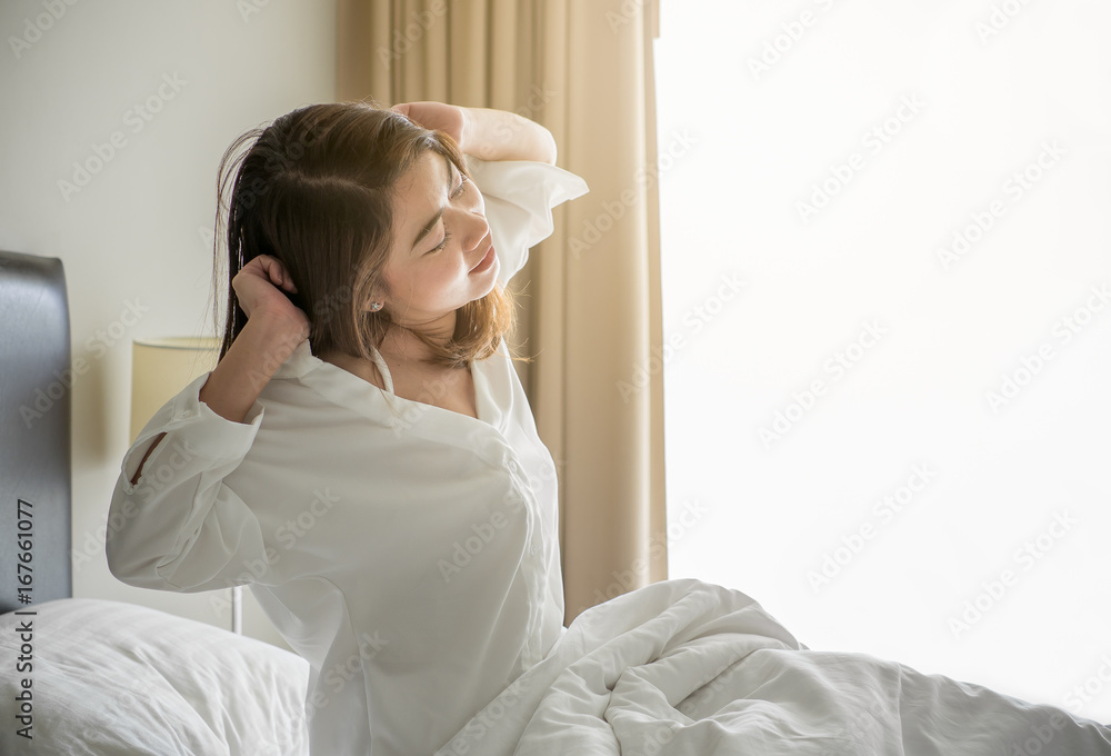 Asian woman wake up in the morning, sitting on white bed and stretching, feeling happy and fresh