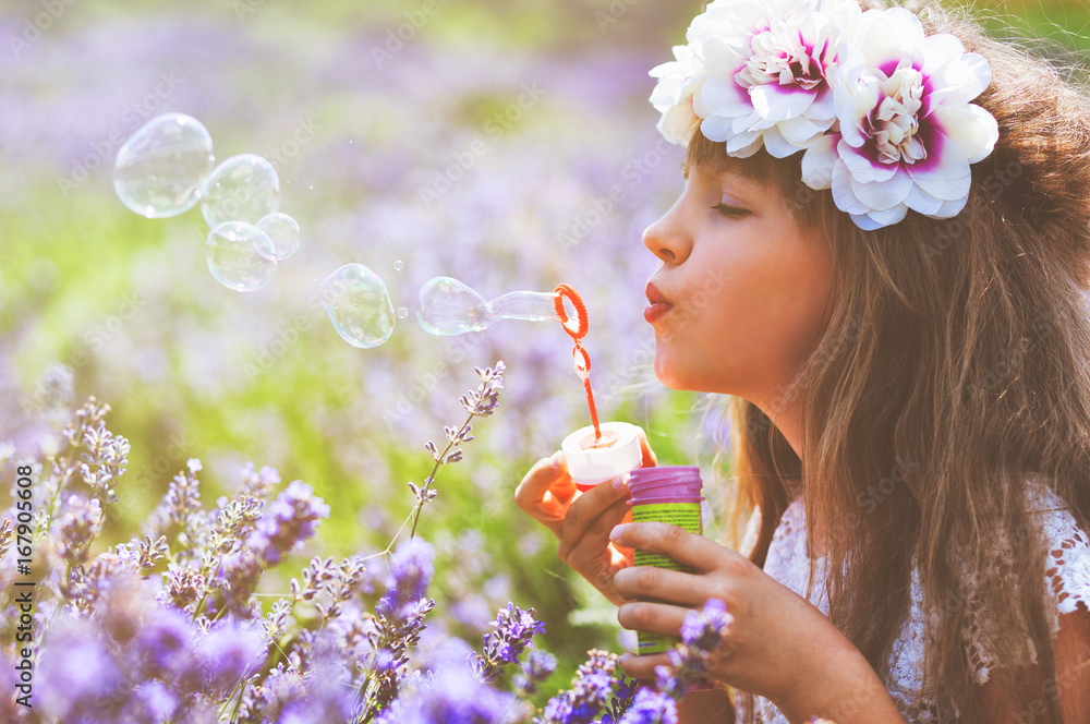 Child girl blowing soap bubbles and having fun in lavender field