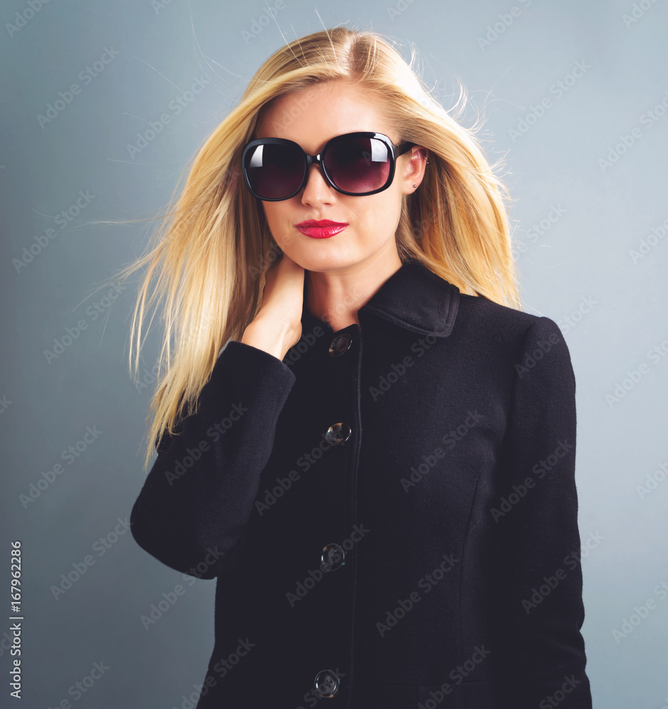  Beautiful young blonde woman in a black coat and sanglasses