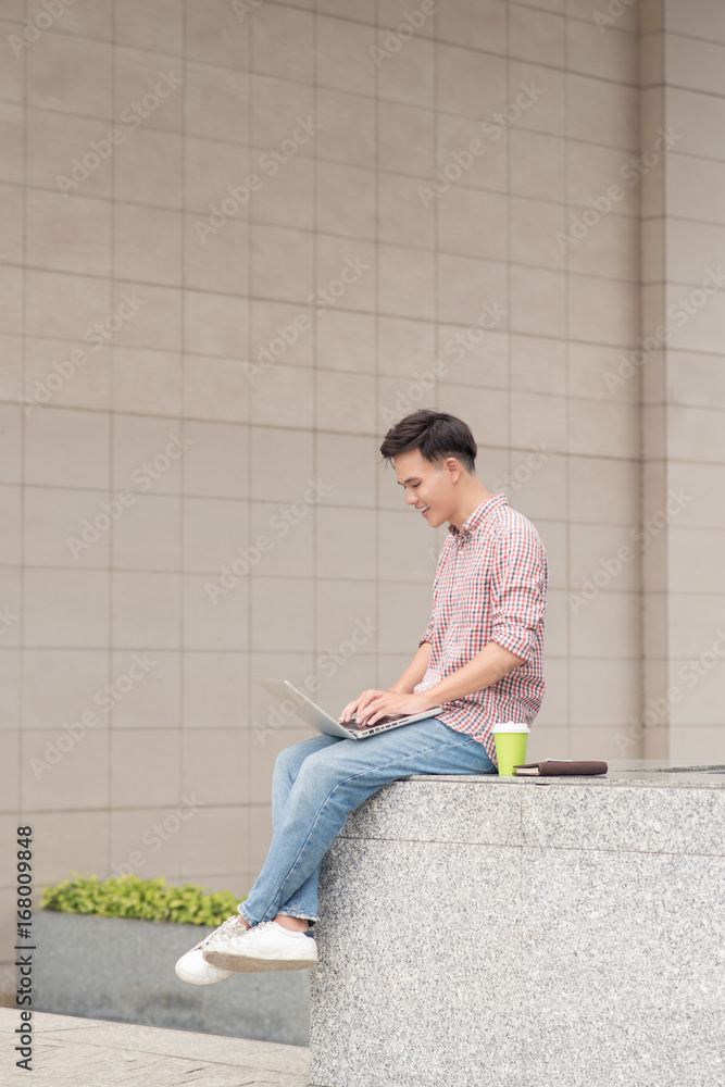 Young man sitting with laptop outside the office