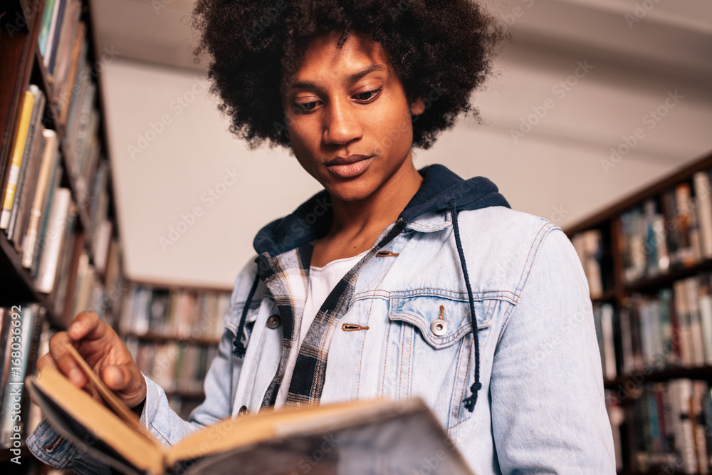 Young student reading a book in library