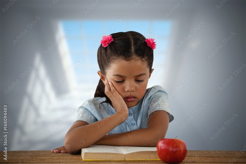 Composite image of concentrated girl reading book at desk