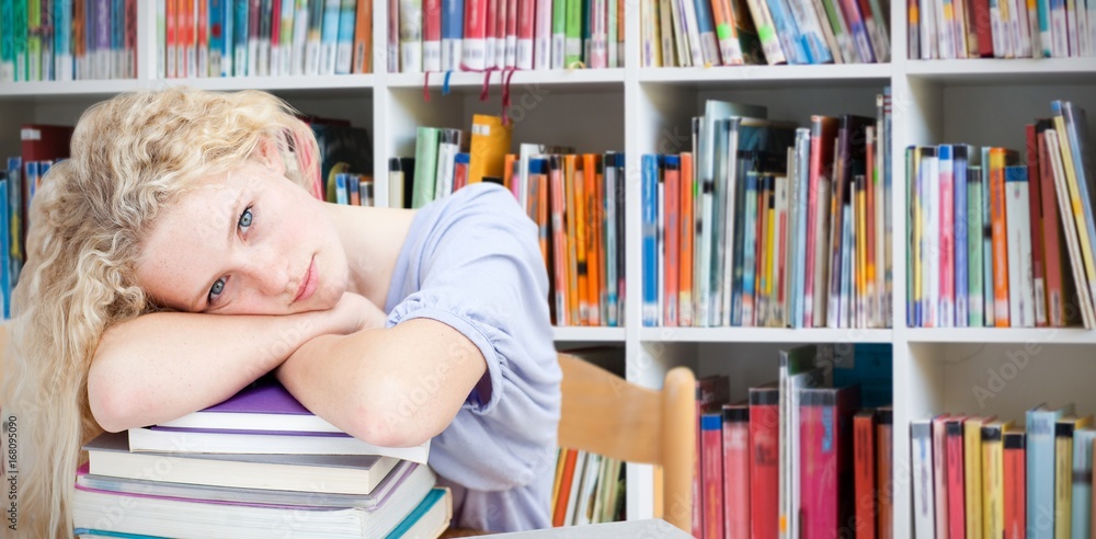 Composite image of tired teeenager sleeping in a library