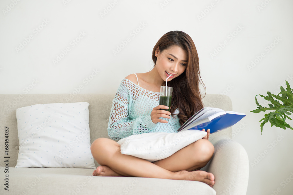 Woman relaxing on sofa in livingroom enjoying reading a book and drinking coffee.