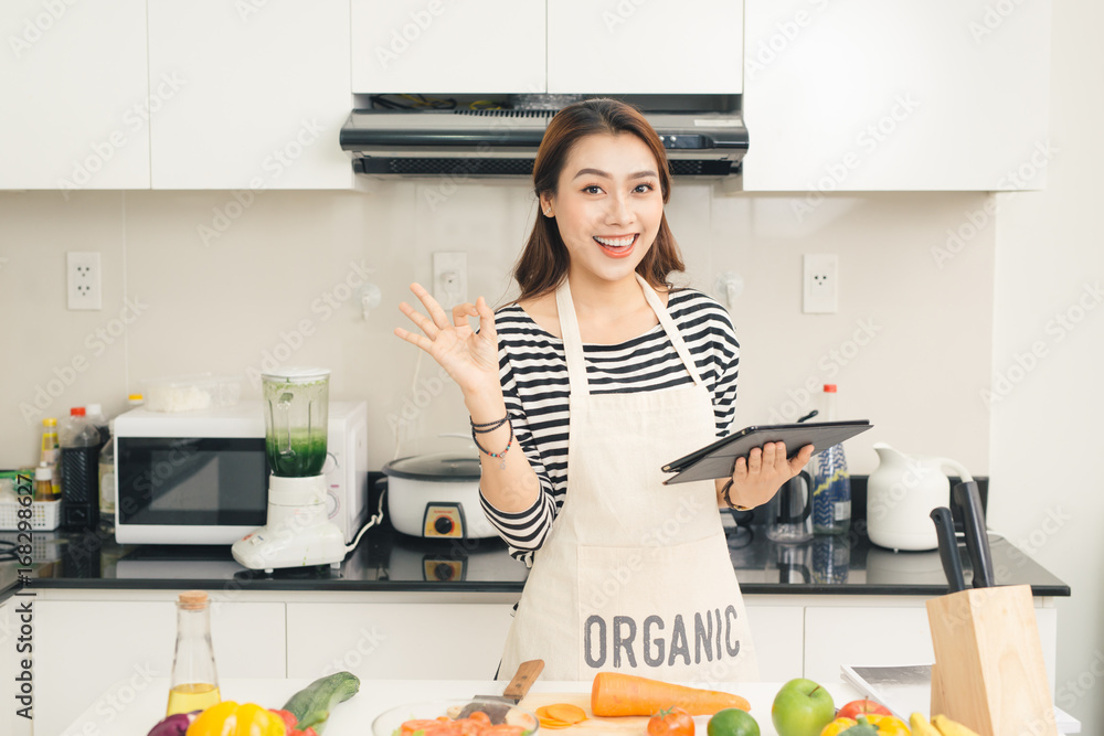 漂亮的年轻家庭主妇，在厨房里用平板电脑做饭