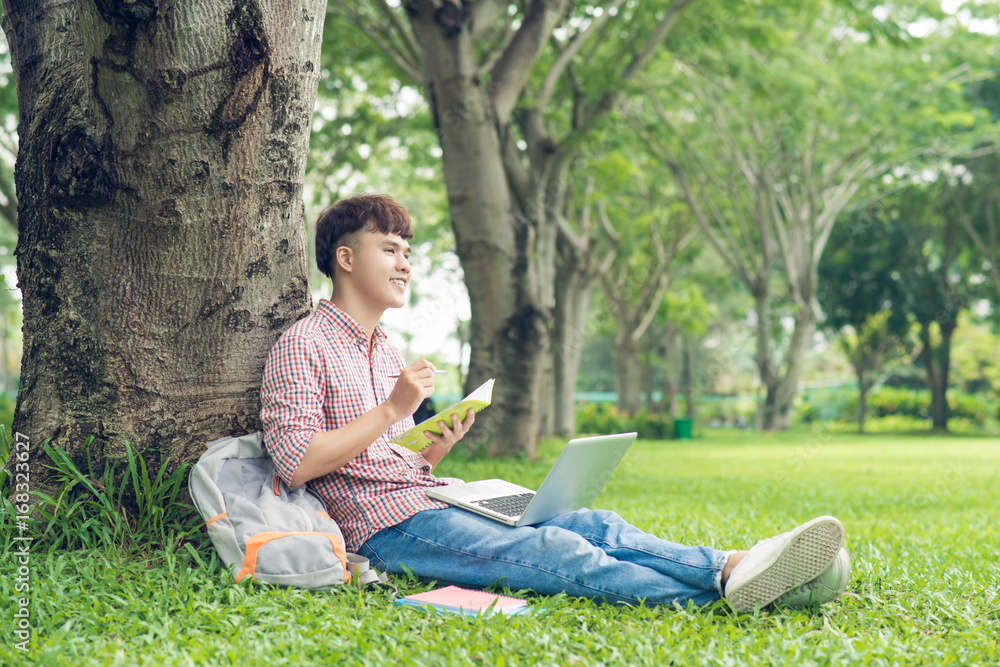 微笑的休闲学生坐在草地上眺望大学校园