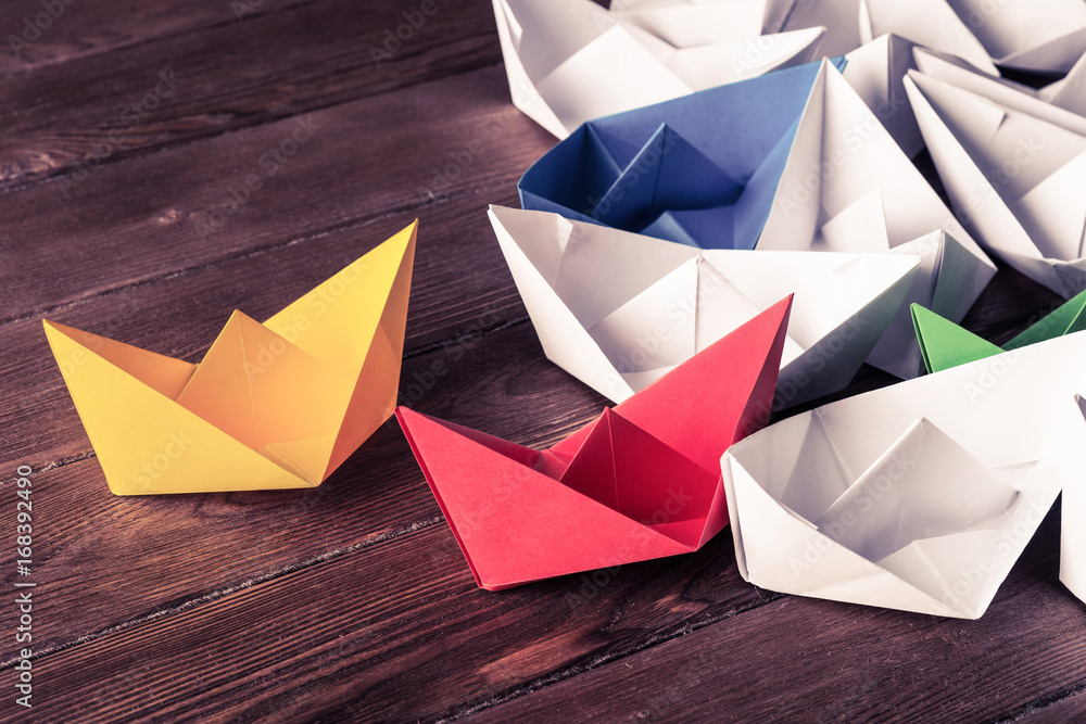 Business leadership concept with white and color paper boats on 