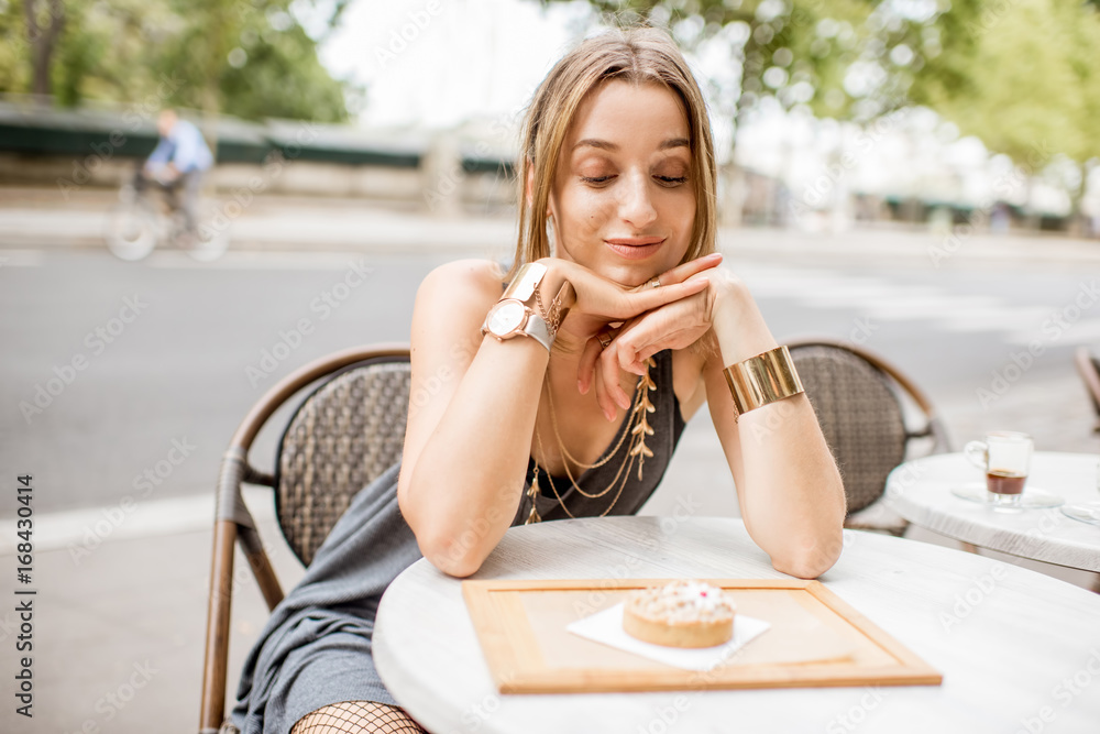 Young pretty woman looking at the sweet cake sitting outdoors at the french cafe