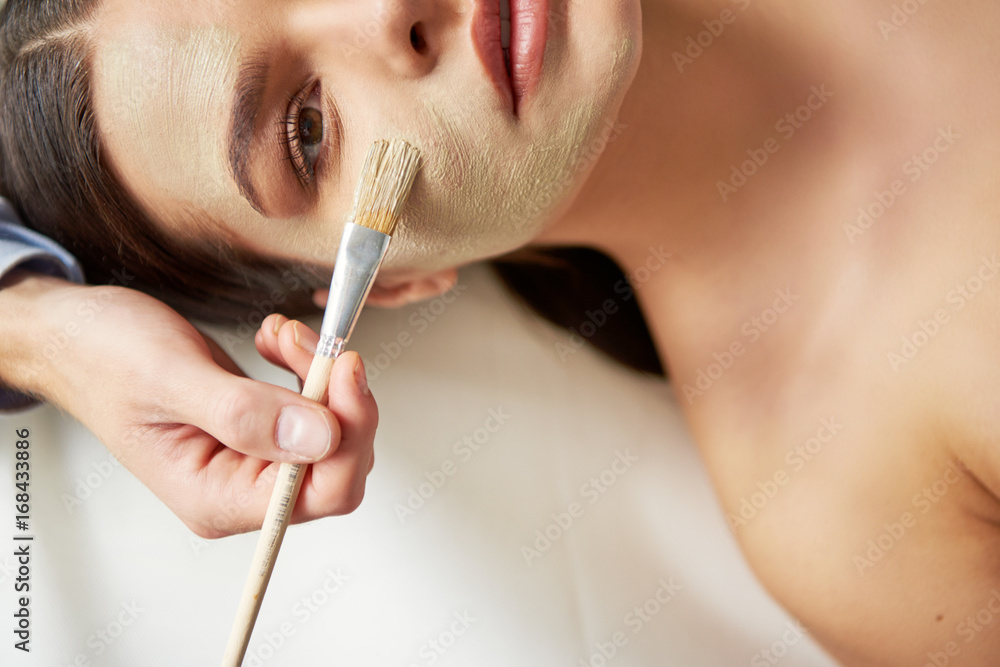 Hand of beauty specialist applying mask on woman with brush