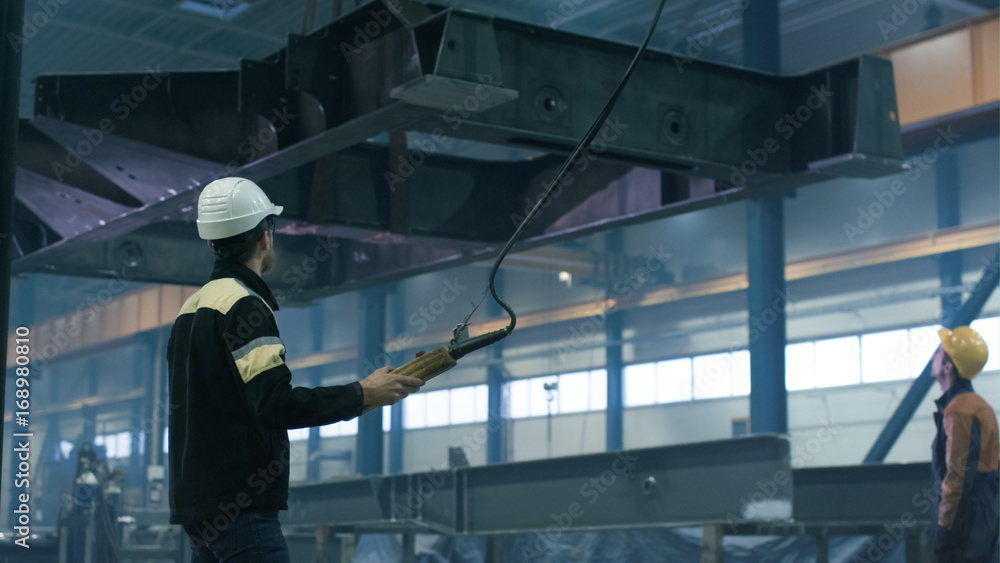 Heavy industry workers are moving a massive metal construction detail in a factory.