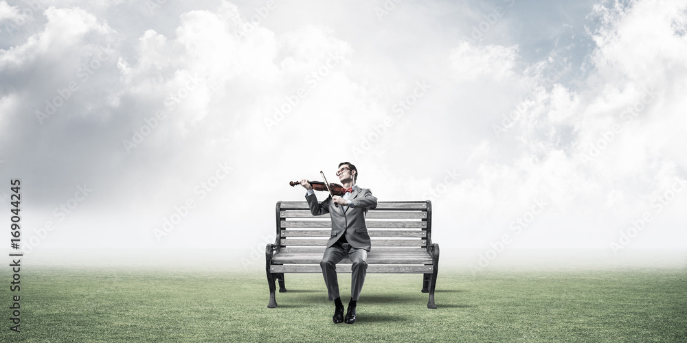 Handsome businessman in park on wooden bench play his melody