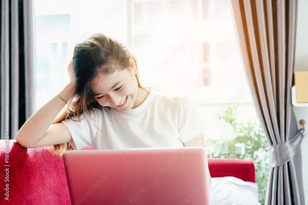 Asian teenage girl using a laptop computer to check her orders online and drinking coffee on a red s