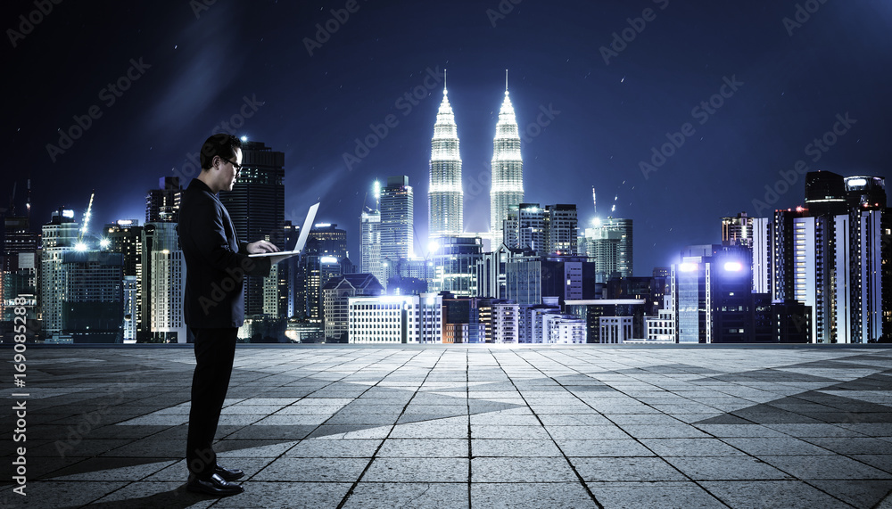 Businessman using laptop with cityscape background , night scene .