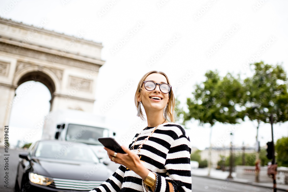 Lifestyle portrait of a young beautiful woman in striped sweater using smart phone on the street in 