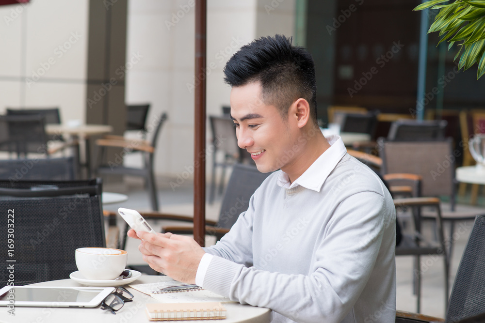 年轻的亚洲快乐男人在咖啡时间用智能手机在社交媒体应用程序上发短信