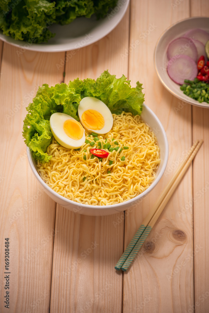 Instant noodles in bowl with vegetables and  boiled egg on wood background