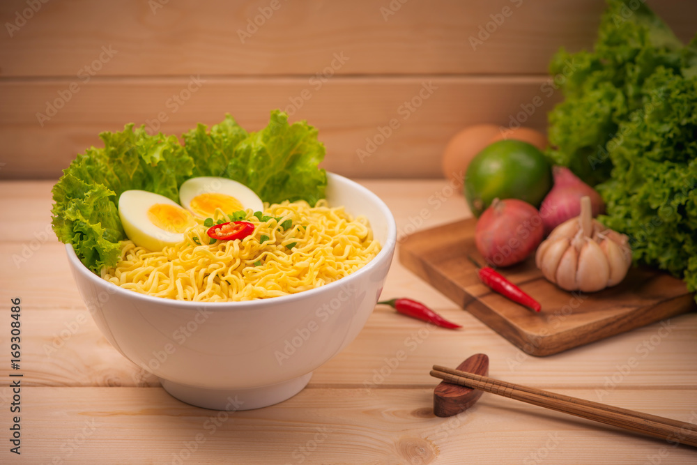 Instant noodles in bowl with vegetables and  boiled egg on wood background