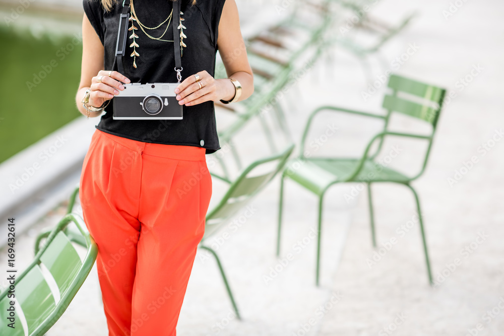 Young stylish woman tourist standing with photocamera near the famous green chairs in Tuileries gard