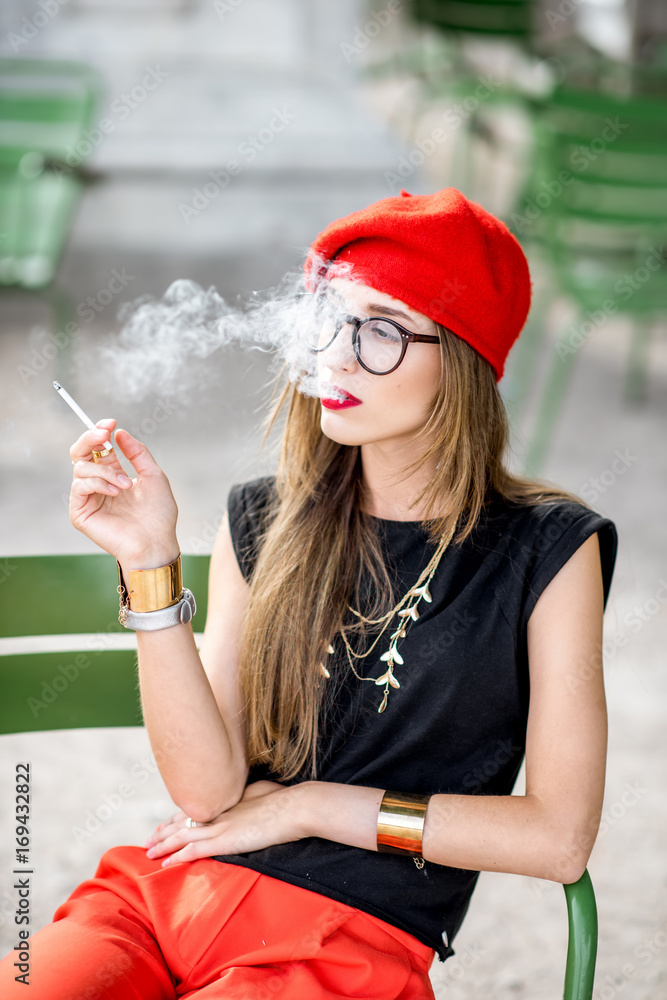 Portrait of a young french woman in red cap smoking cigarette outdoors