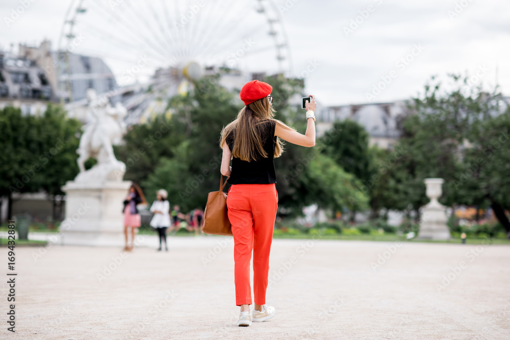 戴着红帽子，穿着红裤子的年轻女子在巴黎杜乐丽公园散步，背景是摆轮